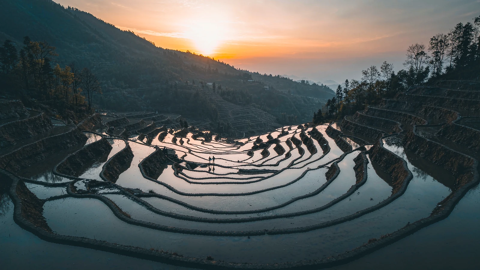 Terraços de arroz de Yuanyang no pôr do sol, com a água dos campos refletindo o céu alaranjado