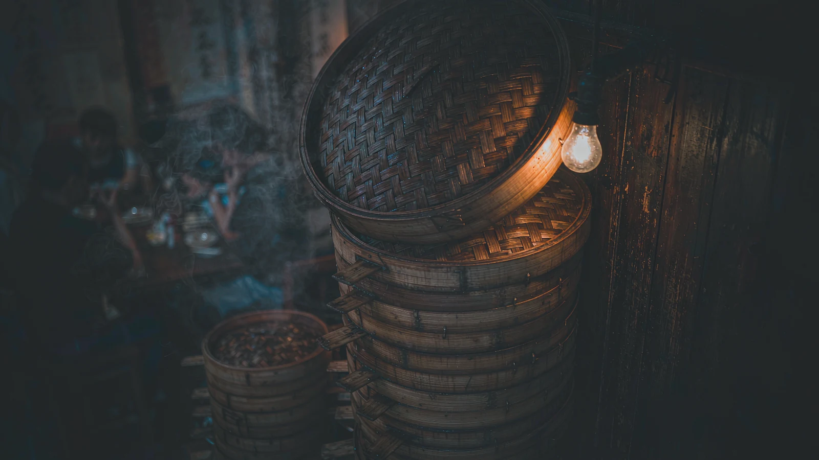 Stacks of bamboo dim sum baskets coming out of the steamers in a Cantonese kitchen