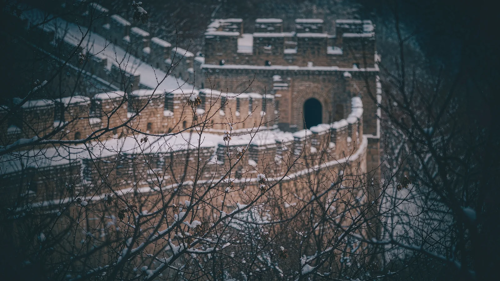 Trecho da Grande Muralha coberto de neve, com a crista branca subindo entre as montanhas