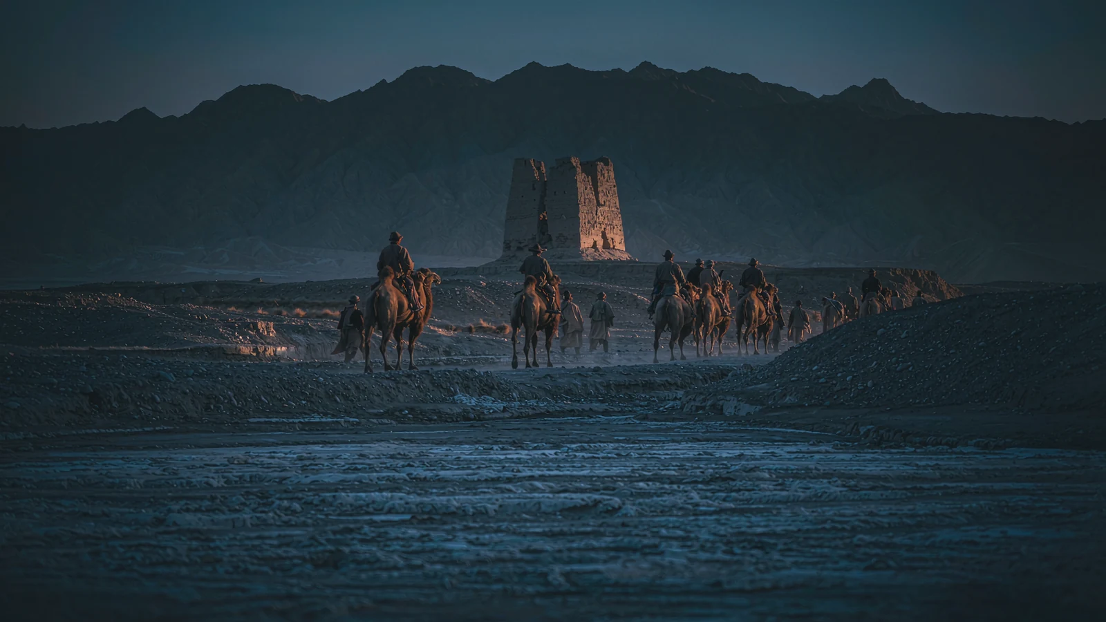 Camel caravan passing an adobe signal tower on the desert edge, on the Silk Road