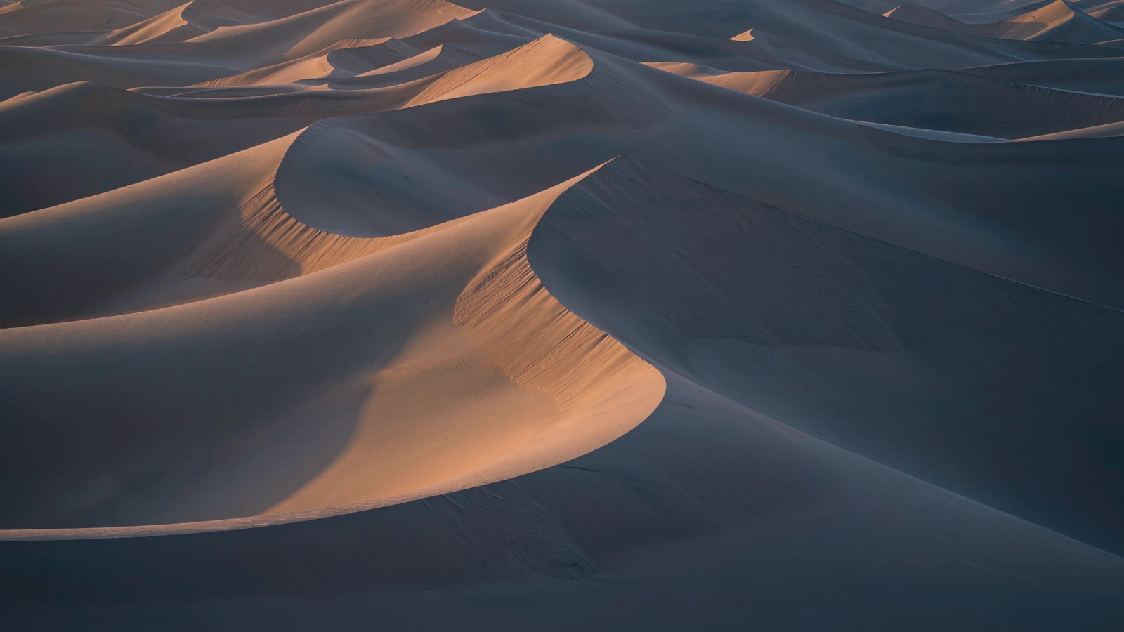 Edge of a desert dune at Mingsha Shan, sand drawn by the wind and Dunhuang in the distance
