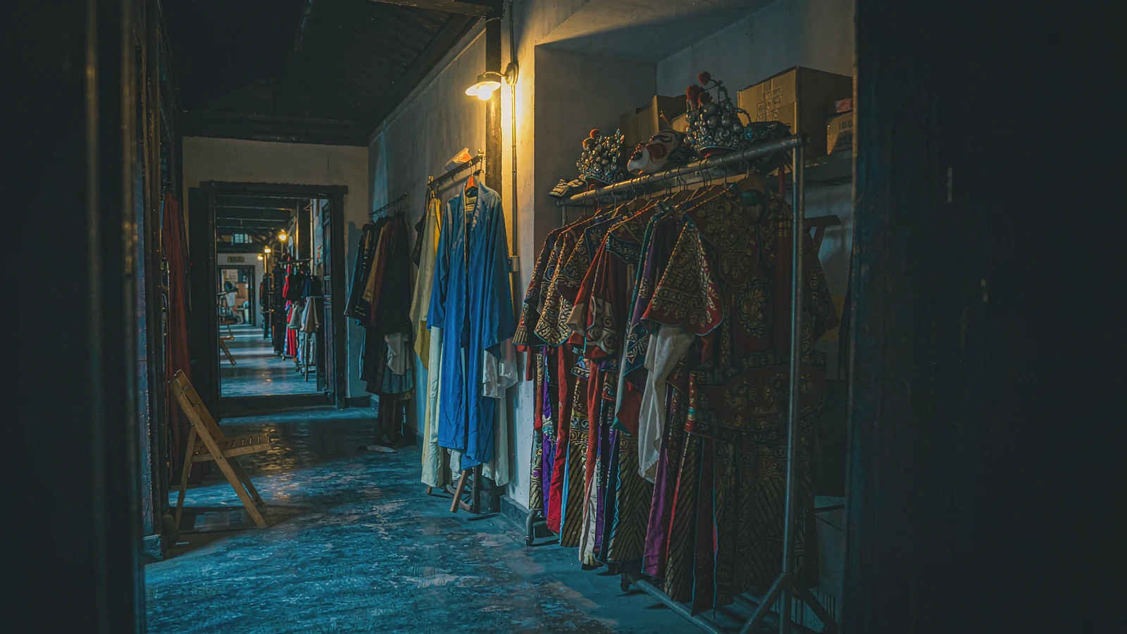 Bastidores de ópera de Sichuan, com máscaras pintadas penduradas e um ator preparando o traje